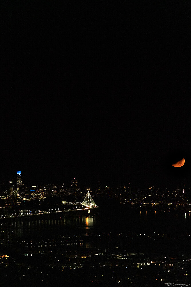 A yellow sliver of the moon sets over the San Francisco Skyline and Bay Bridge, CA