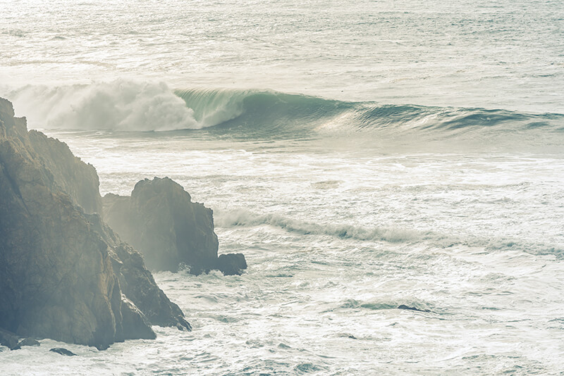 A large wave breaking off shore highlighted by a golden glow at Gray Whale Cove Beach, CA