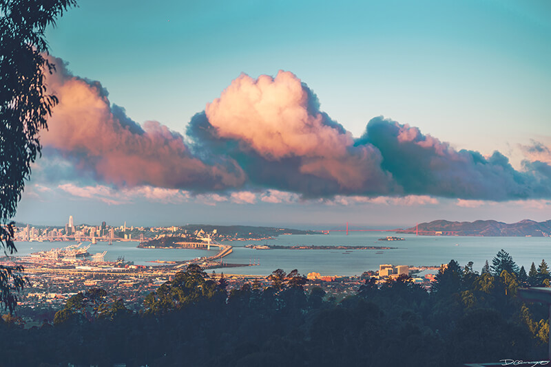 Big fluffy pink and orange clouds float over the San Francisco Bay Bridge, seen from Berkeley's Grizzly Peak Overlook, CA