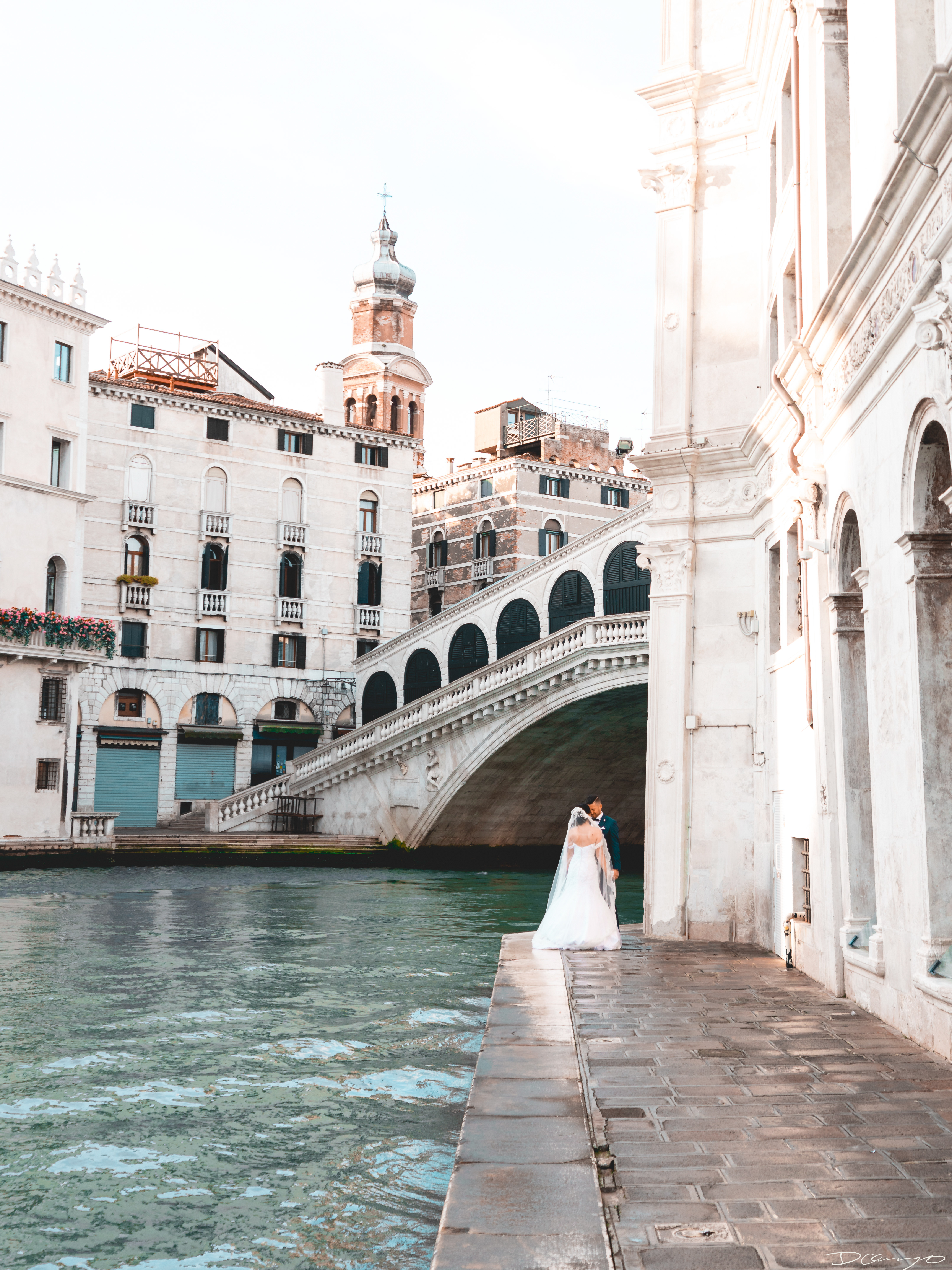 A newly wed couple standing on a walkway under the Rialto Bridge in Venice, Italy.